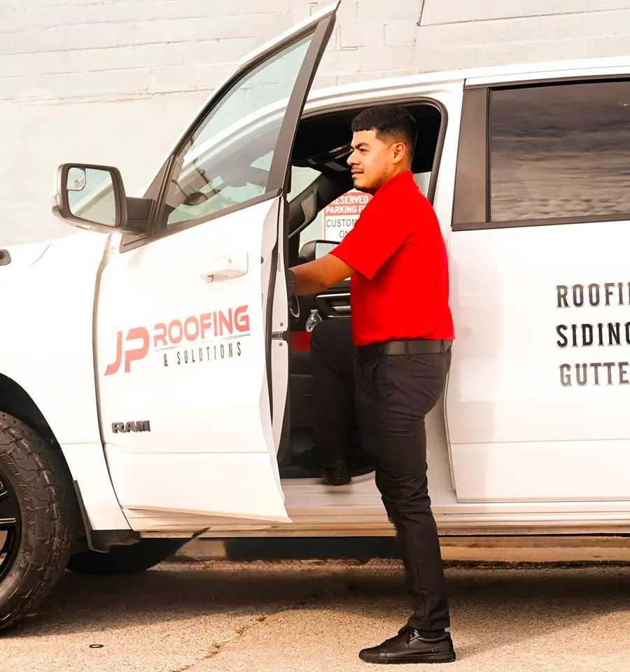 Man in a red shirt getting into a white truck with "JP Roofing & Solutions" logo. The scene conveys professionalism and readiness for work.